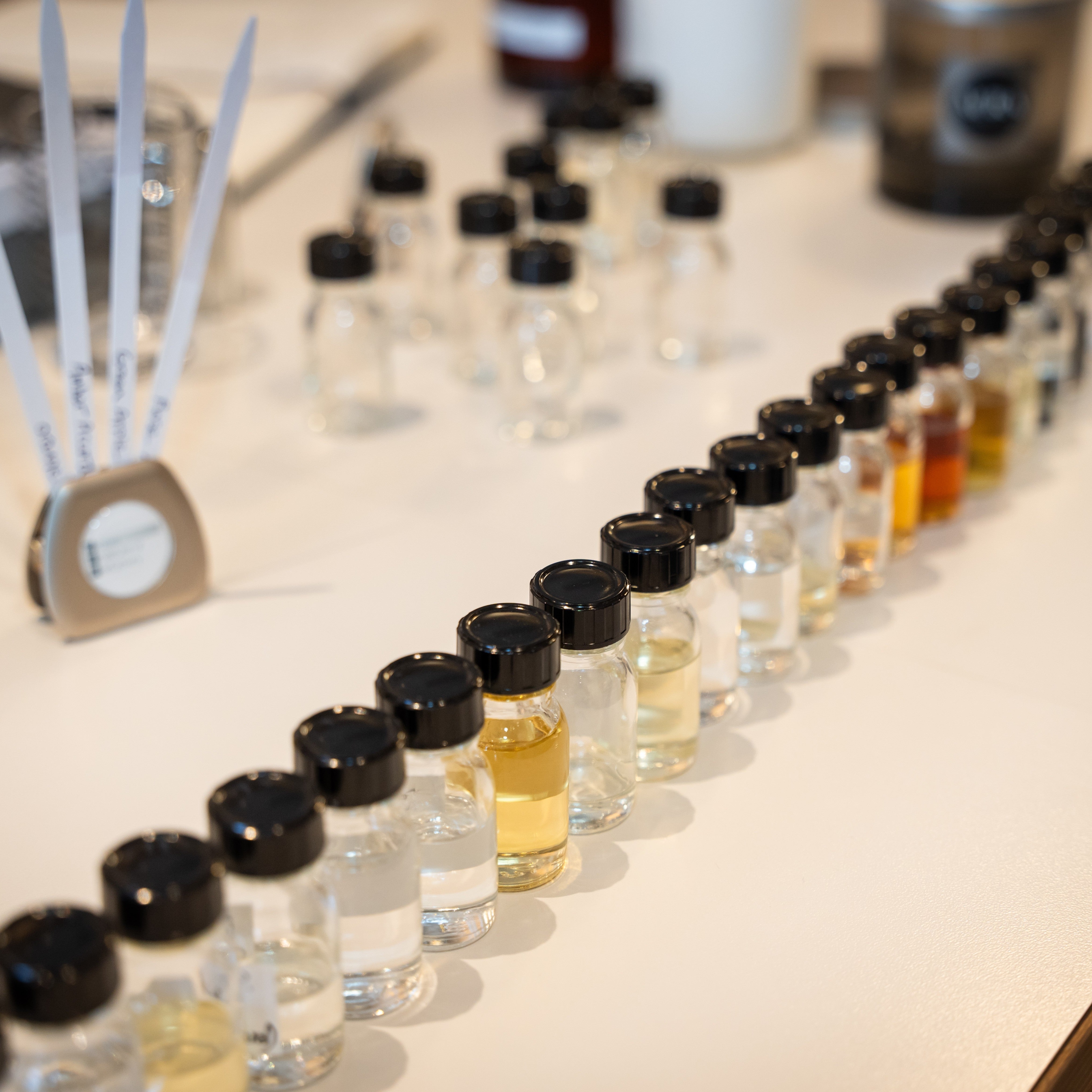 Individual fragrance raw materials in glass vials with black lids.  Paper smelling strips, scale and other perfumer's materials to make fragrance laid out on a light color counter top
