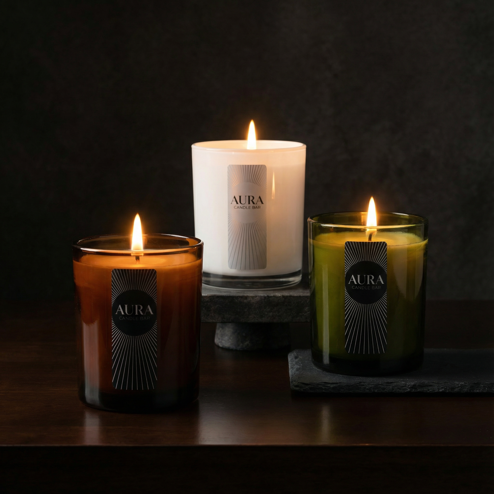 Lit AURA Candle Bar Signature Fragranced Candles- AURA Winter in vintage green glass vessel, AURA Coastal Verde in glossy white glass vessel and AURA Oud Noire in an amber glossy vessel